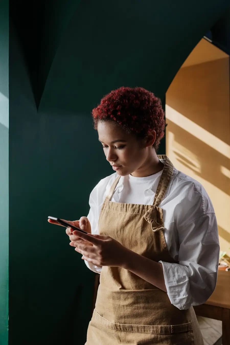 Profissional de avental consultando o celular em um pequeno ambiente de trabalho
